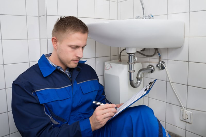A plumber writing on a clip board while doing an inspection