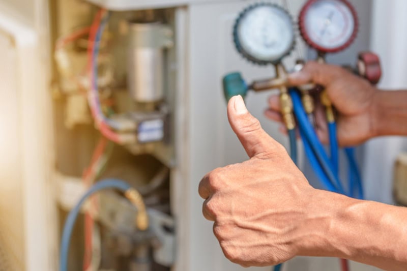 Repairman on the floor fixing air conditioning system, giving a thumbs up.